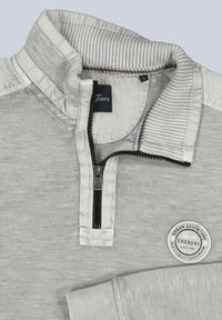 Hellgrauer Zip-Pullover mit strukturiertem Stoff, geripptem Kragen und Bündchen sowie einem runden Logo-Patch auf der Brust mit "Urban Adventure."
