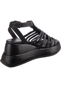 Černé kožené klínové sandály s otevřeným popruhovým designem. Mají silnou podrážku a hladkou texturu. Opatřeny nastavitelným popruhem kolem kotníku pro bezpečné uchycení.