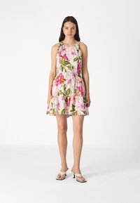 Blumenkleid mit tailliertem Oberteil und elastischem Bund, mit rosa und grünen Mustern auf hellem Hintergrund. Getragen mit beigen Sandalen.