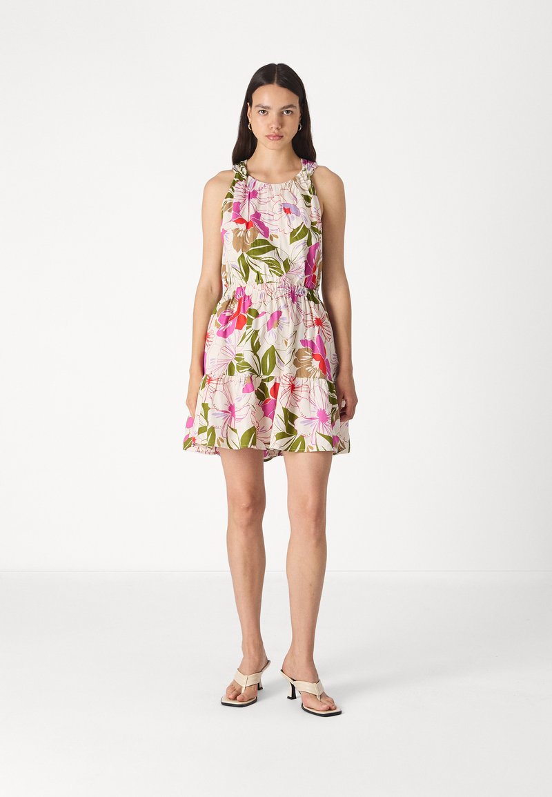 Blumenkleid mit tailliertem Oberteil und elastischem Bund, mit rosa und grünen Mustern auf hellem Hintergrund. Getragen mit beigen Sandalen.