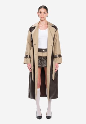 Beiger und brauner Trenchcoat mit strukturiertem Design, langen Ärmeln und offenem Vorderteil. Getragen über einem weißen Oberteil und einem braunen Minirock.