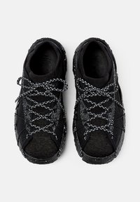 Black athletic shoes with white speckled laces and soles, knit fabric upper, viewed from top on a white background.