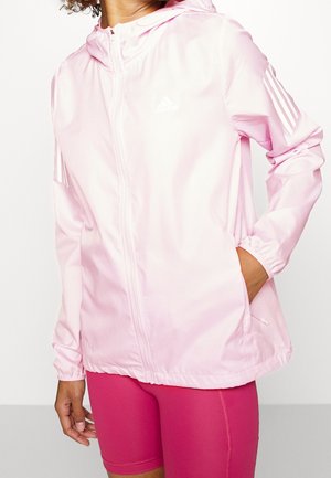 Lyserød zip-up jakke lavet af letvægtigt stof, med hætte, elastiske håndled og hvid Adidas-logo på brystet samt tre striber på ærmerne.