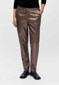 Metallische, roségoldene Hosen mit schlankem Schnitt, die über Seitentaschen und eine glatte, glänzende Textur verfügen. Kombiniert mit schwarzen Slippern.