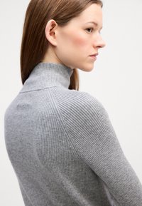 Grauer gerippter Rollkragenpullover aus strukturiertem Stoff, taillierte Passform und subtile Nahttdetails, seitlich dargestellt.