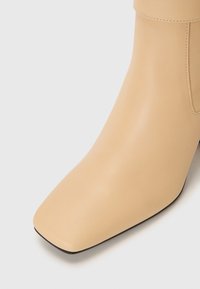 Bottine en cuir beige à bout carré, avec un design minimaliste et une texture lisse, ornée de coutures subtiles.