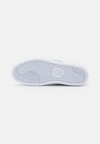 Sole di sneaker bianca con motivo a presa testurizzato, bordi curvi e un'impronta circolare del logo; materiale in gomma liscia con una leggera lucentezza.