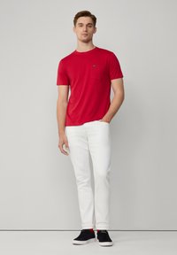 Rode katoenen T-shirt met korte mouwen en een zak, gecombineerd met witte slim-fit jeans en zwarte sneakers met rode accenten.