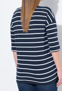 Marinblå och vit randig topp med trekvartsärmar, avslappnad passform och axelsnitt. Mjuk bomullsmaterial, jämn textur.