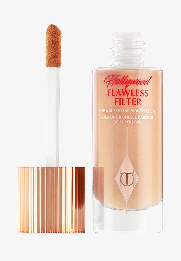 Durchsichtige Flasche mit flüssigem Highlighter in einem hellbeigen Farbton, einem gerippten rose goldenen Deckel und einem weichen Applikationsstab. Roter Text auf dem Etikett.