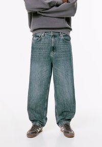 Svijetloplave široke traperice s izblijedjelim završetkom, s pet džepova i kopčanjem na gumbe. Uparene s smeškim sportskim cipelama.