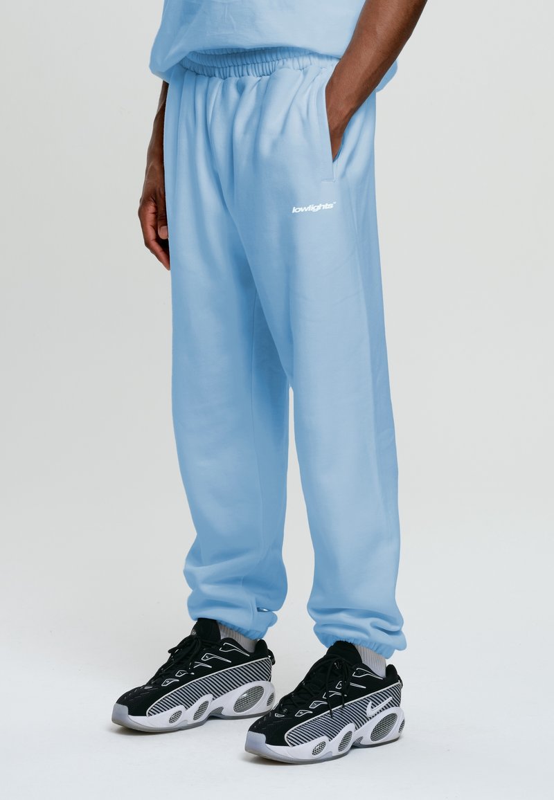 Hellblaue Sweatpants mit elastischem Bund und Seitentaschen, darauf in Weiß der Schriftzug "lowlights". Kombiniert mit schwarzen und weißen Sneakern.