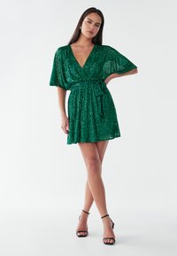 Roheline sära kleit V-kaelusega, lühikeste varrukatega ja nööritud vöökohaga. Laienev seelik, mis on sileda tekstuuriga ja vabalt liikuv.