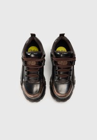 Sapatilhas pretas e castanhas com um acabamento brilhante, atacadores texturizados, colar almofadado e bico arredondado. Apresentam um logótipo circular na língua.