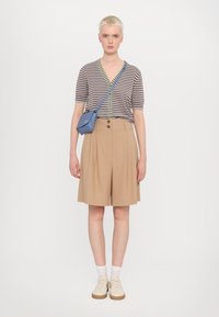 Striped short-sleeve top with green accents, beige pleated shorts, paired with cream sneakers and a blue crossbody bag. Smooth textures.