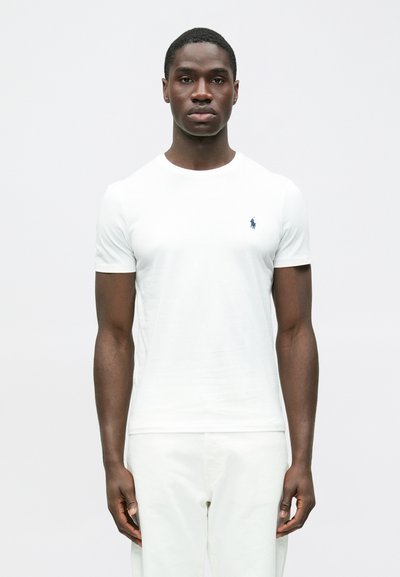 Biele bavlnené tričko s krátkymi rukávmi, okrúhlym výstrihom, s malým námorníckym logom na ľavej strane hrudníka, hladkou textúrou a priliehavým strihom.