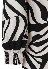 Detail eines schwarz-weiß gestreiften Stoffes mit einem gepufften Ärmel und elastischem Bündchen. Das Material wirkt baumwollähnlich mit einer leicht strukturierten Oberfläche.