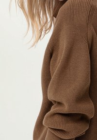 Pull marron tricoté avec texture côtelée, coupe décontractée, épaules tombantes, mettant en valeur un tissu doux et épais ainsi que des poignets retroussés.