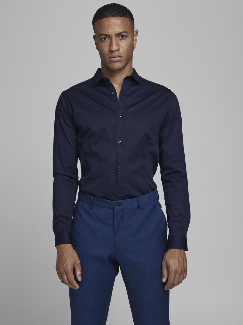 Navy blue cotton shirt with a fitted design, long sleeves, button placket, and contrasting cuffs; paired with blue tailored trousers.
