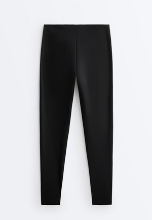 Černé legíny s vysokým pasem, úzkým střihem, bezešvým designem a hladkou, pružnou texturou látky.