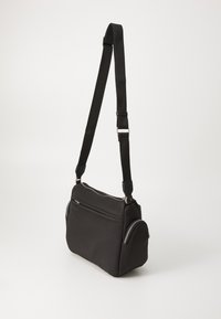 Borsa a spalla in tessuto nero con tracolla regolabile, scomparti con zip, forma strutturata e texture liscia. Dettaglio notevole della tasca laterale.