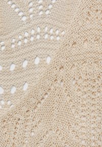 Coperta in maglia color beige chiaro, con motivi a foglia in pizzo, texture morbida e design leggero e arioso.