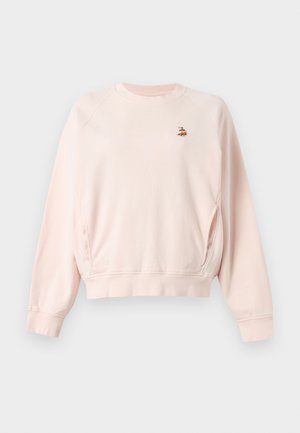 Personne portant un sweat-shirt rose clair avec un petit emblème d'abeille, une jupe crème longueur genou, des chaussures marron avec des nœuds, et des lunettes de soleil œil de chat, debout.
