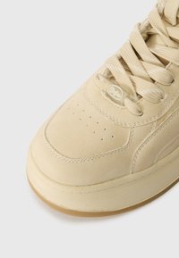 Μπεζ αθλητικά με ομαλή σουέντ επένδυση, στρογγυλή μύτη, επίπεδα κορδόνια, τρύπες για αερισμό και καουτσούκ σόλα. Ετικέτα με λογότυπο κοντά στα κορδόνια.