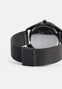 Sorthævet stål ur med mesh rem. Rundt ansigt og en poleret spænde. Bagsiden viser specifikationer og mærkenavn.