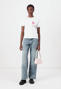Witte katoenen t-shirt met een roze graphic, gecombineerd met lichtblauwe wijde jeans en een roze handtas. Schoeisel is zwart met platform.