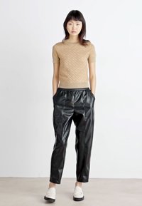 Beige rakstainā īsām piedurknēm top, melnas mākslīgās ādas sašaurinātas bikses un baltas slip-on kurpes ar biezu zoli. Minimālisma dizains, gluda tekstūra.