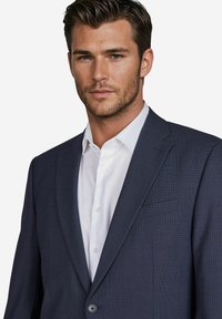 Donkerblauwe textuur blazer met enkele knoopsluiting, pieklapels en een borstzak, gedragen over een wit overhemd met knopen.