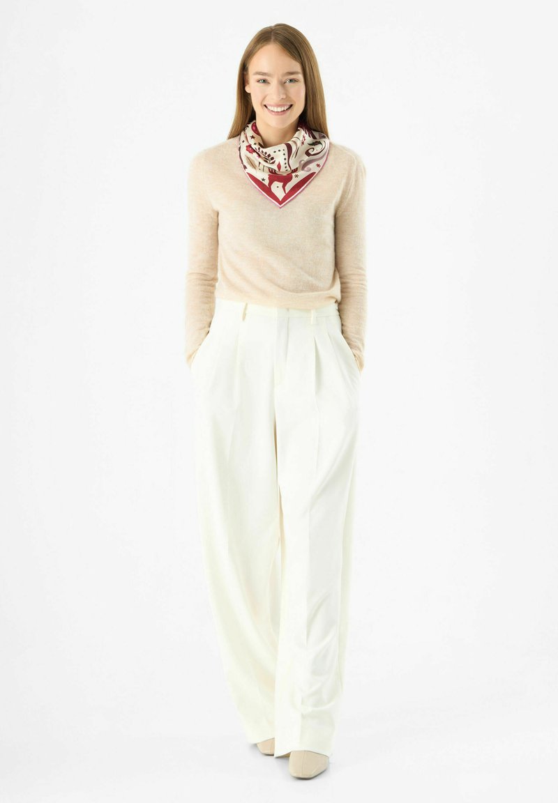 Pull beige clair avec un décolleté flatteur, assorti à un pantalon blanc à taille haute et jambes larges, accompagné d'une écharpe à motifs aux tons crème et rouge.