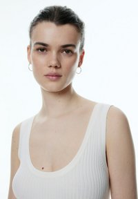 Witte geribbelde tanktop met een ronde halslijn en brede schouderbanden. Gladde textuur met een minimalistisch ontwerp zonder patronen of accenten.