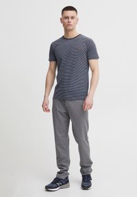 Striped navy T-shirt with a round neckline, paired with gray sweatpants. Model wears blue athletic shoes. Textured fabric, casual fit.