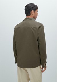 Herenshirt in olijfgroen met een ontspannen pasvorm, lange mouwen en een klassieke kraag. Gemaakt van soepel materiaal, met knoopmanschetten en een achterste yoke.