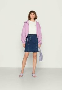 Sweatshirt roxo, t-shirt branca com texto colorido, saia de ganga escura, bolsa lilás e chinelos. Textura suave, design casual.