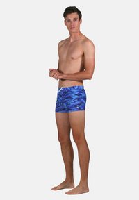 Shorts de bain camouflage bleus en tissu léger, avec une taille à cordon de serrage et une texture lisse. Coupés au-dessus du genou.