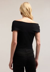Top negro sin mangas con textura suave, diseño ajustado y mangas cortas, combinado con pantalones negros que tienen bolsillos traseros.