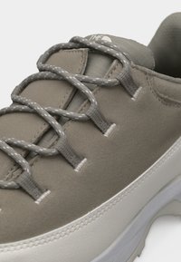 Κοντινό πλάνο ταουπέ αθλητικού παπουτσιού με κορδόνια σε γκρι σχέδιο, επενδεδυμένη γλώσσα και λευκή υφή στην σόλα.