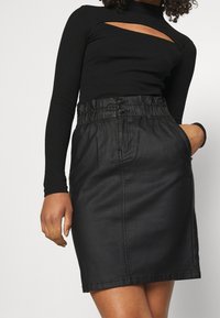 Jupe en denim noir avec une taille élastique, comprenant deux boutons, des poches latérales et une coupe droite. Haut noir à manches longues avec détail découpé.