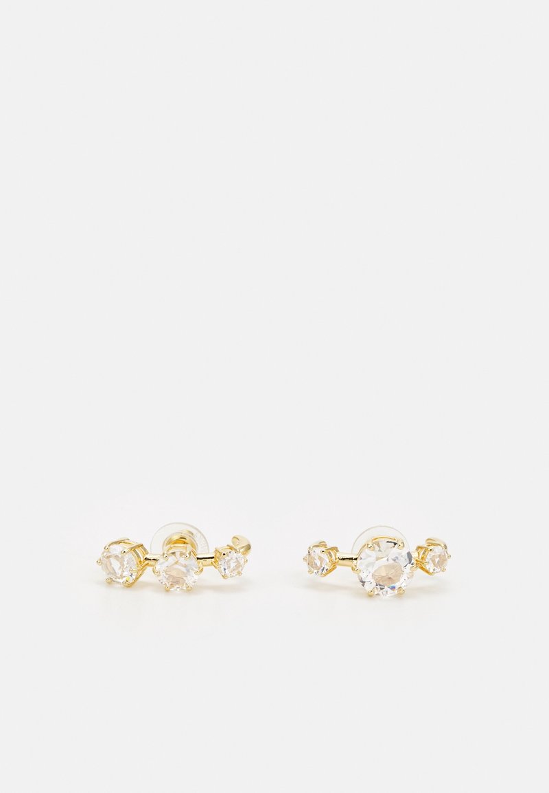 Boucles d’oreilles clous en or avec trois pierres précieuses rondes et claires de tailles variées disposées en ligne courbée et support transparent.