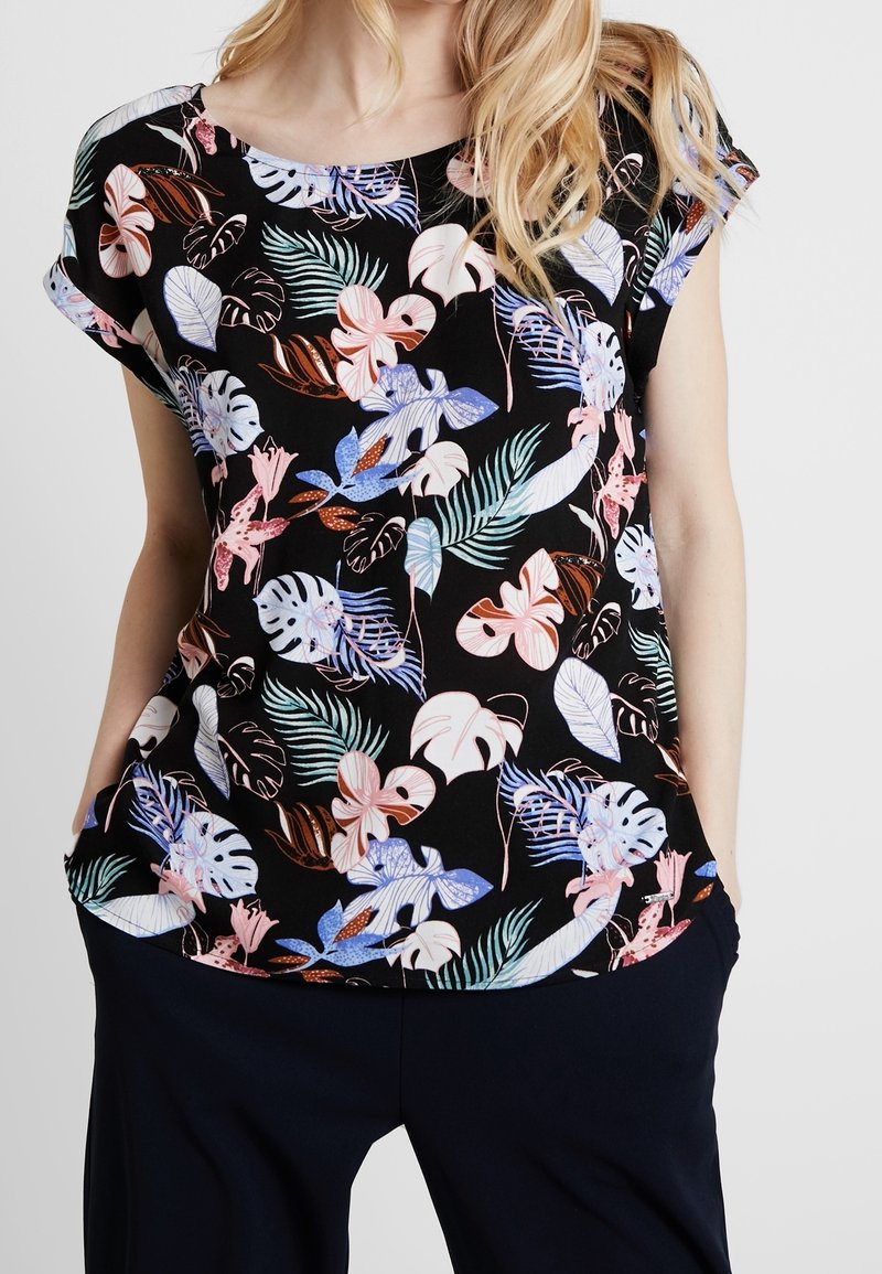 Haut floral à manches courtes, avec un fond noir. Le motif inclut des feuilles colorées en tons de bleu, rose et vert. Texture douce.