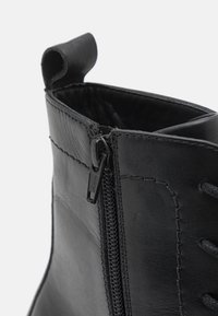 Bottine en cuir noir avec fermeture éclair sur le côté, couture renforcée et une boucle au col pour un enfilage facile. Texture lisse avec une finition mate.