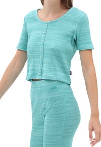 Un haut court côtelé bleu sarcelle à manches courtes, avec un col rond et une fermeture à boutons, assorti à un pantalon côtelé.