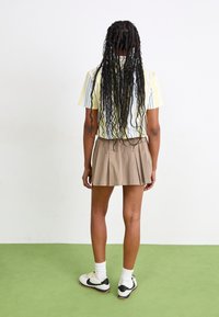Camicetta a righe con maniche corte nei toni del giallo e blu chiaro, abbinata a una gonna plissettata color khaki, indossata con calze bianche e sneakers con dettagli neri.