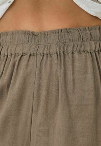 Pantalons en lin marron avec une taille élastique froncée, tissu texturé et coupe ample, montrant les détails des coutures et des plis du tissu.