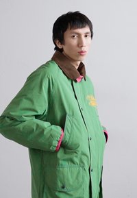 Grøn isoleret jakke med brun krave, pink detaljer og to frontlommer. Har knaplukning og en afslappet, løs pasform.