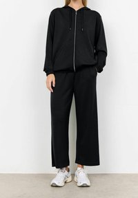 Černý teplákový komplet s mikinou na zip a širokými kalhotami vyrobenými z měkké tkaniny, s volným střihem a elastickými manžetami.
