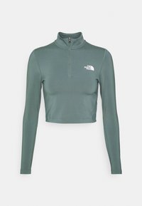 Beschnittenes Langarmoberteil aus verblasstem grünen Polyester mit einem Stehkragen und halbem Reißverschluss, ausgestattet mit einem weißen Logo auf der linken Brust.